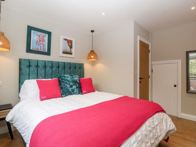 A bedroom with a bed with teal headboard white bedding and pink pillows a wooden door and small white door on the wall at Sevenwoods View in Longhope