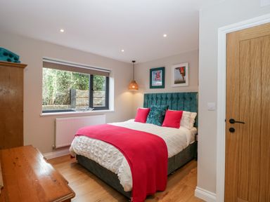 A bedroom with a bed with red pillows and throw a wooden cabinet and a window at Sevenwoods View in Longhope