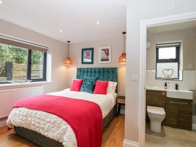 A bedroom with a bed with red and teal pillows beside a bathroom with a toilet and sink at Sevenwoods View in Longhope