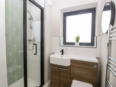 A bathroom with a shower enclosure a sink wooden cabinets a window and a circular mirror at Sevenwoods View in Longhope
