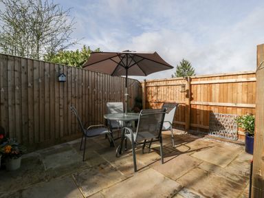 An outdoor patio with a glass table four chairs a large umbrella and wooden fencing at Sevenwoods View in Longhope