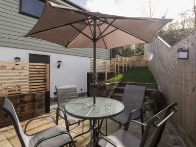 A patio with a glass table and four chairs under a large umbrella at Sevenwoods View in Longhope
