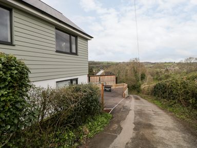 A side view of a house with bushes along a narrow road and a sign reading Sevenwoods View in Longhope