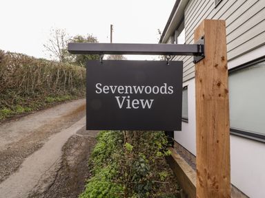 A black sign with white text reading Sevenwoods View mounted on a wooden post next to a road and a building at Sevenwoods View in Longhope