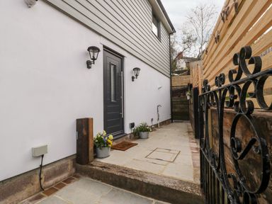 A patio area with a black door wall lights flower pots and wooden and metal fencing at Sevenwoods View in Longhope