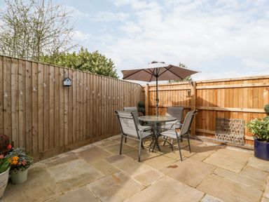 A patio area with a glass table and four chairs under an umbrella and wooden fencing at Sevenwoods View in Longhope