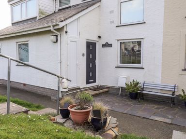 An exterior entrance of a white house with a black door and a bench with potted plants at The Summerhouse in Y Felinheli