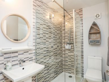 A bathroom with a sink and round mirror next to a glass shower enclosure and a toilet with a boat shaped wall shelf at The Summerhouse in Y Felinheli