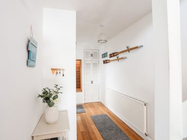 A hallway with wooden floor and white walls featuring a small table with a vase of flowers and wall-mounted oars at The Summerhouse in Y Felinheli
