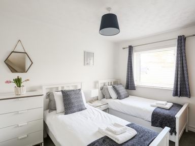 A bedroom with two single beds a dresser and a window with curtains at The Summerhouse in Y Felinheli