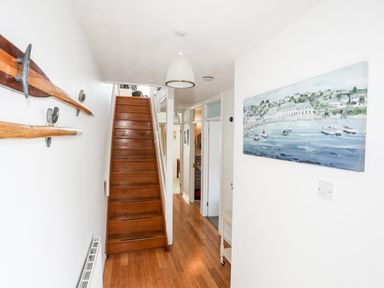 A hallway with wooden stairs and hardwood floor with oars mounted on one wall and a painting of boats on water on the other wall at The Summerhouse in Y Felinheli