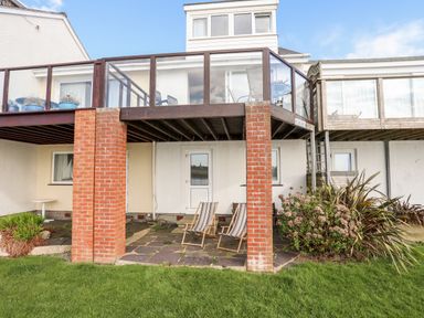 An outdoor patio with two striped deck chairs under a wooden balcony supported by red brick pillars at The Summerhouse in Y Felinheli