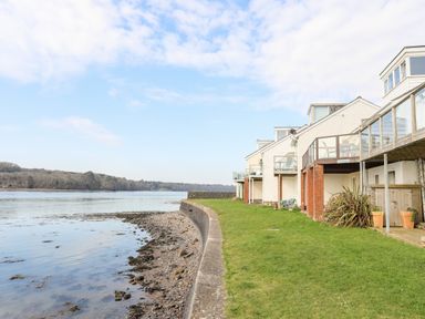 A row of houses with balconies along a shoreline with grass and water at The Summerhouse in Y Felinheli
