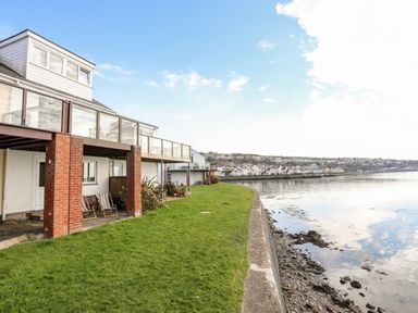 A waterfront property with a patio and glass balcony overlooking a body of water at The Summerhouse in Y Felinheli