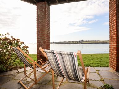 Two striped deck chairs on a stone patio overlooking a grassy area and a body of water at The Summerhouse in Y Felinheli
