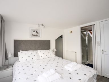 A bedroom with a bed with white bedding with bird prints two bedside lamps and a small bathroom at The Summerhouse in Y Felinheli