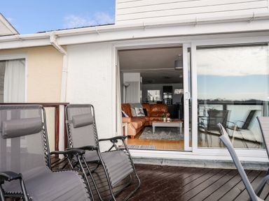 A patio with reclining chairs and a view into a living room with a brown sofa and coffee table at The Summerhouse in Y Felinheli