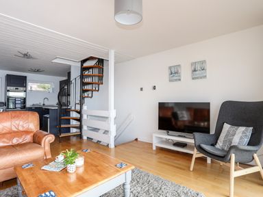 A living room with a leather armchair a wooden coffee table a gray armchair a television on a white stand and a spiral staircase at The Summerhouse in Y Felinheli