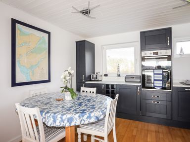 A kitchen with a round dining table covered with a blue and white tablecloth and white chairs near dark cabinets with built in oven at The Summerhouse in Y Felinheli