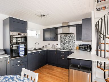 A kitchen with dark cabinets a built-in oven a mosaic tile backsplash and a spiral staircase at The Summerhouse in Y Felinheli