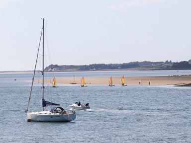 A sailboat and a motorboat on the water near a sandy beach with small sailboats and people at The Summerhouse in Y Felinheli