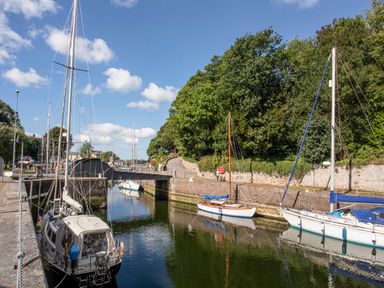 A small canal with sailboats moored on each side and a footbridge with trees along the right bank at The Summerhouse in Y Felinheli