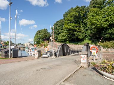 A small bridge over a canal with boats docked along the sides and trees in the background at The Summerhouse in Y Felinheli