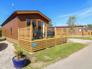 A wooden lodge with a deck and outdoor seating in a grassy area at Eden Lodge - Sherwood 21 in South Lakeland Leisure Village