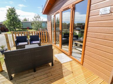 An outdoor wooden deck with black wicker seating and glass doors leading inside at Eden Lodge - Sherwood 21 in South Lakeland Leisure Village