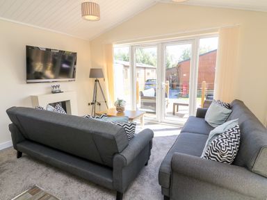 A living room with two gray sofas a wooden coffee table a floor lamp and a wall-mounted television at Eden Lodge - Sherwood 21 in South Lakeland Leisure Village