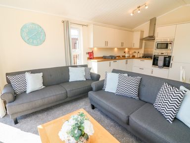 A living room with two gray sofas and cushions next to a kitchen with white cabinets at Eden Lodge - Sherwood 21 in South Lakeland Leisure Village
