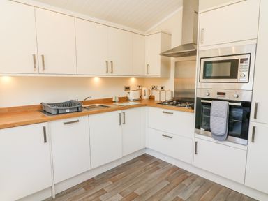A kitchen with white cabinets wooden countertops a sink a dish rack a kettle toaster a gas stove a microwave and an oven at Eden Lodge - Sherwood 21 South Lakeland Leisure Village