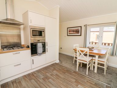 A kitchen and dining area with white cabinets wooden countertops a gas stove built in microwave and oven a wooden dining table with four white chairs and a window at Eden Lodge - Sherwood 21 in South Lakeland Leisure Village