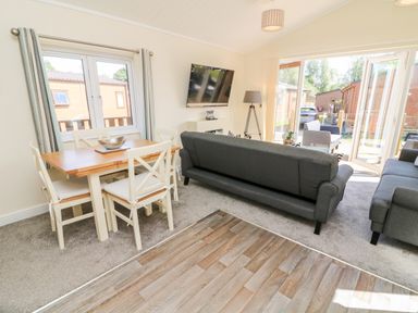 A living room with gray sofas a dining table with four chairs and a wall mounted tv at Eden Lodge - Sherwood 21 in South Lakeland Leisure Village