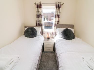 A bedroom with two single beds with gray round cushions and a nightstand with a lamp between them at Eden Lodge - Sherwood 21 in South Lakeland Leisure Village