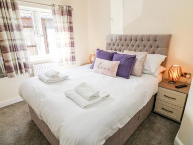 A bedroom with a bed with folded towels bedside tables a lamp and curtains at Eden Lodge - Sherwood 21 in South Lakeland Leisure Village