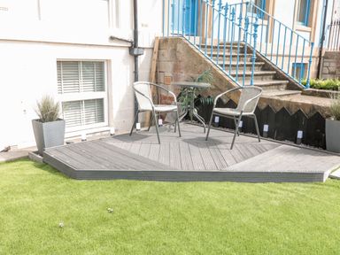 A small patio with two chairs and a round table on a wooden deck with potted plants and stairs in the background at Sunset View in Whitby
