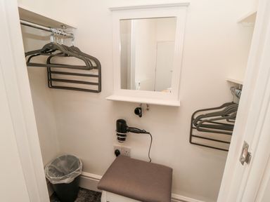 A small dressing room with hangers on rails a mirror a hairdryer a cushioned stool and a trash bin at Sunset View in Whitby