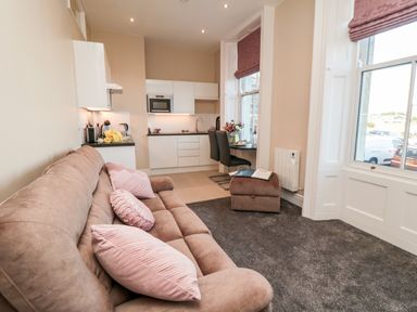 A living area with a brown sofa and pink cushions next to a small kitchen and dining table by windows at Sunset View in Whitby