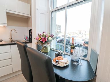 A kitchen with black countertop seating two black chairs and items including flowers food and drink on the table at Sunset View in Whitby
