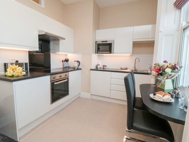 A kitchen with white cabinets black countertops a built-in oven microwave sink and a table with chairs and flowers at Sunset View in Whitby