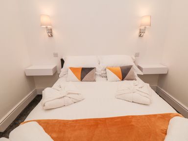 A bedroom with a double bed white bedding two geometric pillows and two wall lamps at Sunset View in Whitby