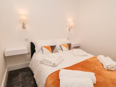 A bedroom with a double bed white linens orange throw pillows and wall lamps at Sunset View in Whitby