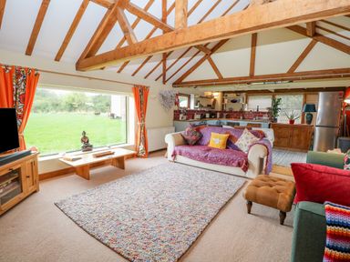 A living room with wooden beams cushions and rug next to a kitchen at The Lodge in Hickling near Catfield