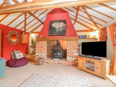 A living room with a brick fireplace wooden beams a television wooden cabinet and a bean bag at The Lodge in Hickling near Catfield