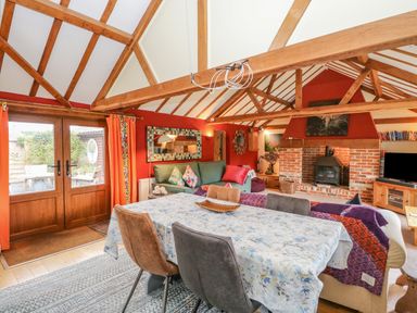 A living room with wooden ceiling beams a dining table chairs a green sofa a brick fireplace and glass doors at The Lodge in Hickling near Catfield