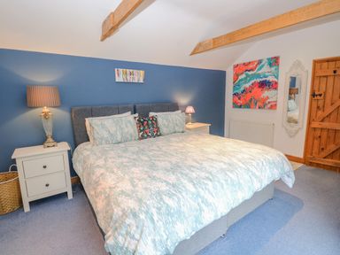 A bedroom with a large bed cushions bedside tables lamps wall paintings and wooden door at The Lodge in Hickling near Catfield