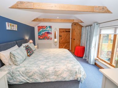 A bedroom with a large bed wooden beams on the ceiling a wooden door and a window with blue curtains at The Lodge in Hickling near Catfield