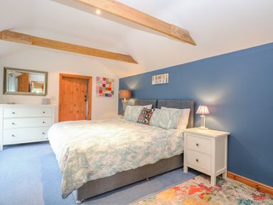A bedroom with a bed between two bedside tables with lamps and a chest of drawers at The Lodge in Hickling near Catfield