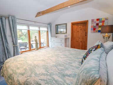 A bedroom with a bed covered in patterned bedding beside a window with curtains and a door with a wooden frame at The Lodge in Hickling near Catfield